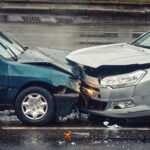 Car accident on wet road during rain, head on collision side view. Two cars damaged after head on collision, car crash. Car crash on the street, damaged cars after collision. Traffic rules violation